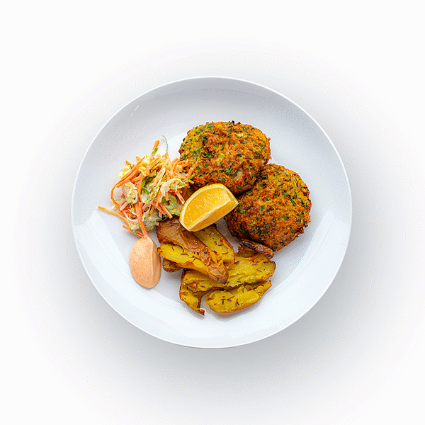 Epicured's Montauk Crab Cakes served with coleslaw, lemon-paprika aioli, and smashed potatoes on a white plate.