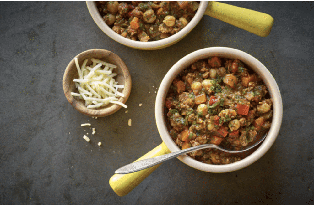 Delicious bowl of Epicured's Three-Spice Turkey Chili with colorful veggies, seasoned meat, and a side of cheddar cheese.